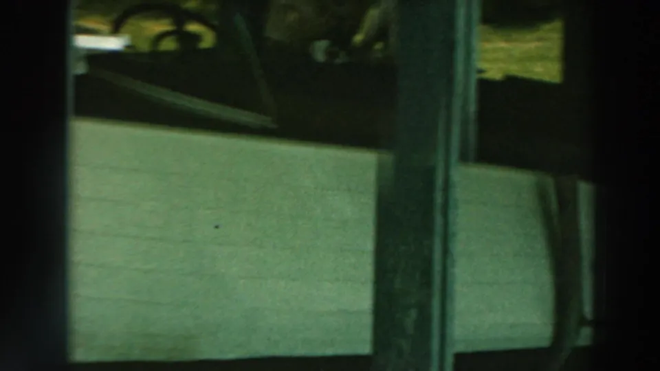 The stored white boat remains partly visible beneath pier framing, with dark supports and muted daylight around the hull.