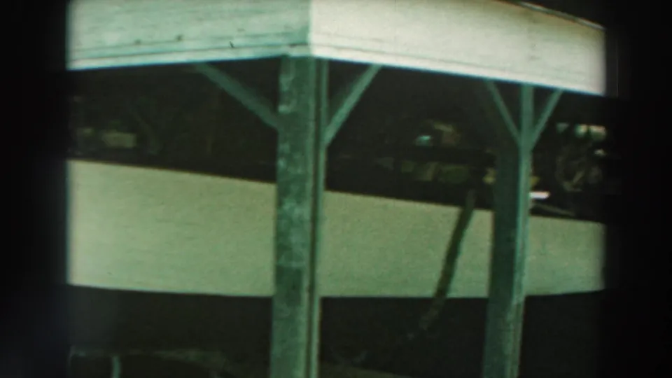 1964 Lake Winnebago home-movie frame showing a boat stored beneath a simple wooden shelter with posts and roof beams.