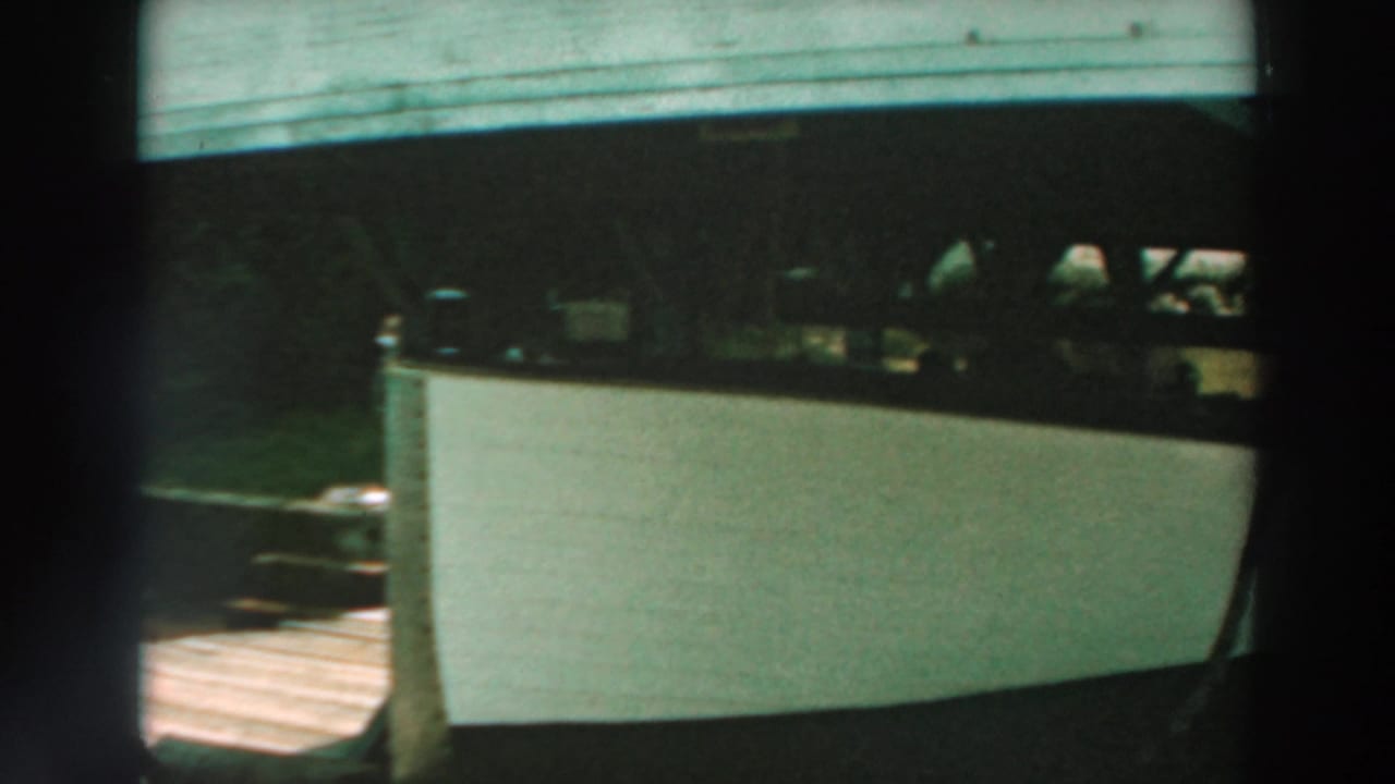 White boat stored under a weathered wooden pier at Lake Winnebago, Wisconsin, in 1964 home-movie footage.