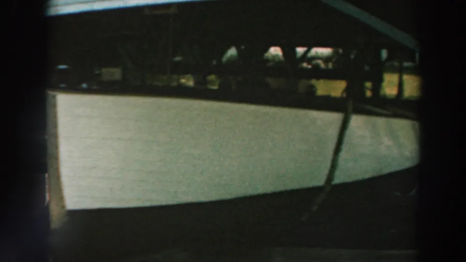 1964 Lake Winnebago home-movie frame showing a white boat stored under a covered lakeside dock.