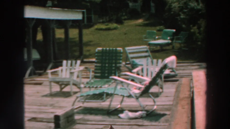 1964 Lake Winnebago home-movie frame showing striped folding lawn chairs on a wooden lakeside deck.
