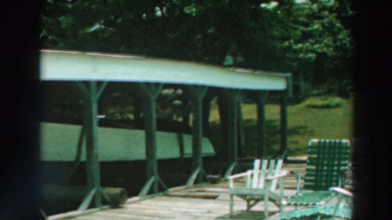 Covered dock structure with white boat underneath and chairs on a wooden deck.