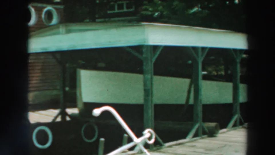 Lake Winnebago home-movie frame showing the covered boat shelter, white boat, dock railing, chair, and partial house exterior.
