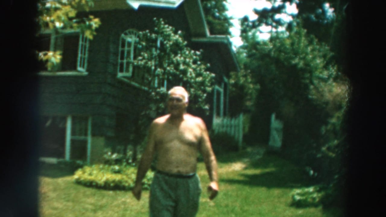 In 1964 Lake Winnebago, Wisconsin footage, an older shirtless man walks through a sunny backyard near a dark-shingled house.