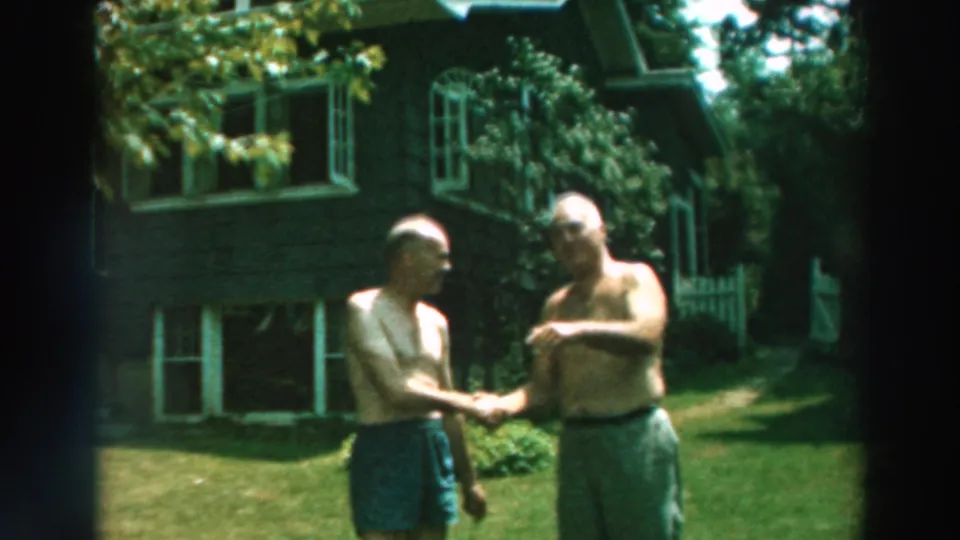 During the backyard handshake, one older man gestures while both stand shirtless near the house and lawn.