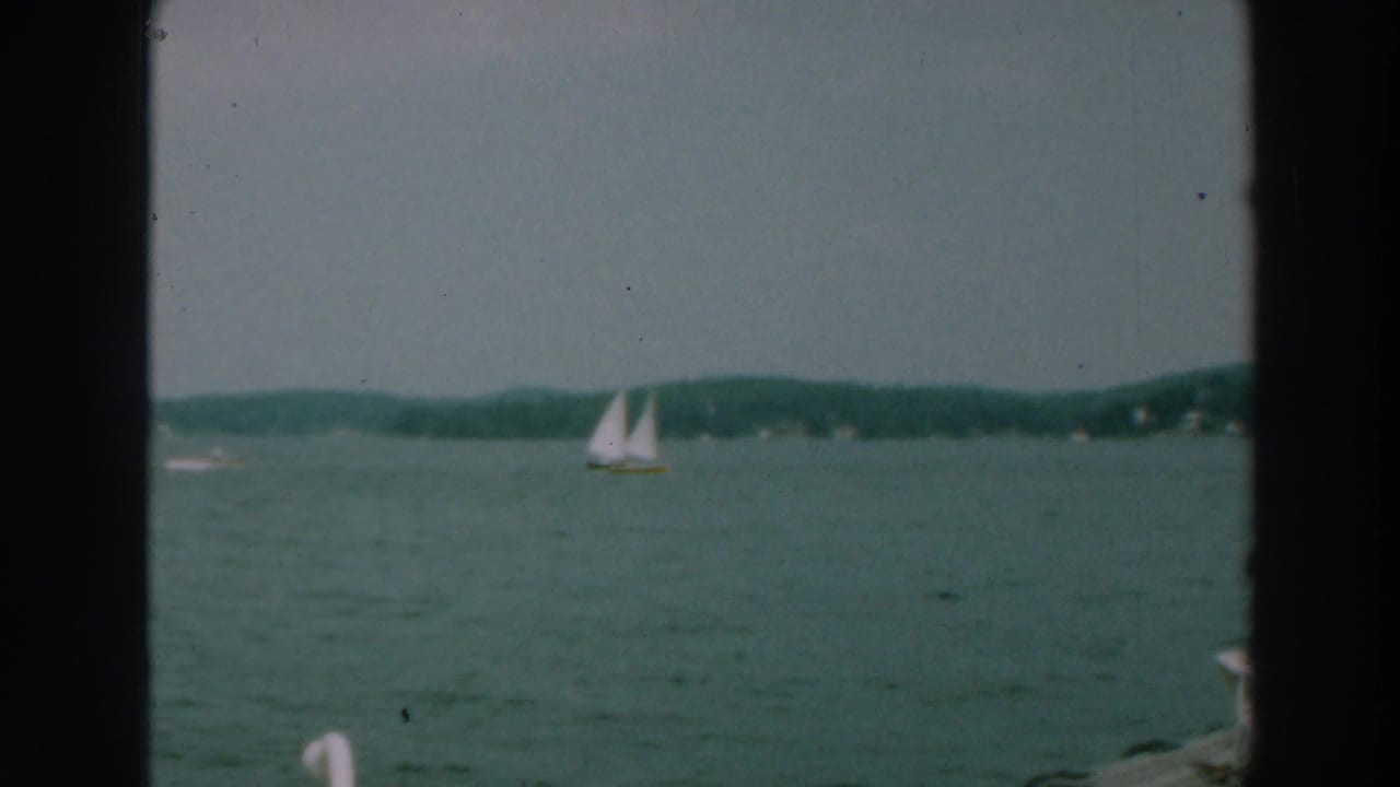 Distant sailboat on open lake water beneath a muted sky.
