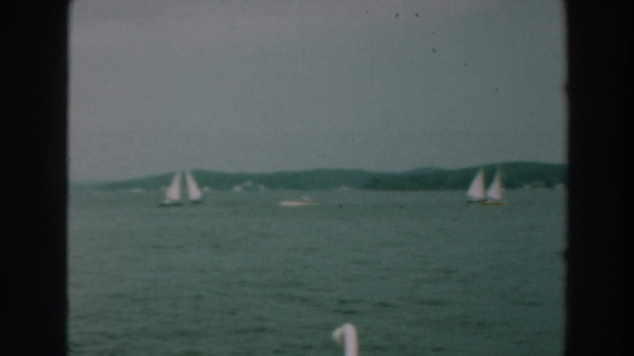 Two distant sailboats on lake water with low hills beyond.