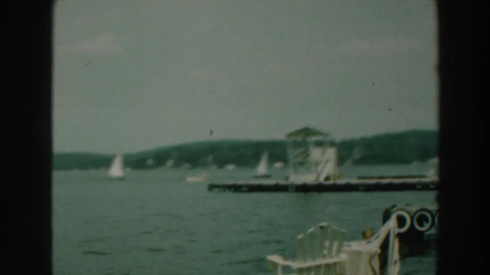 Lake Winnebago shoreline footage shows small sailboats beyond a dock or raft and foreground lakefront chairs.