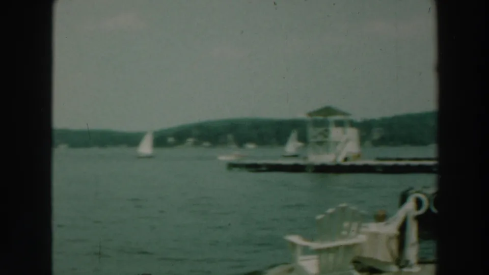 A 1964 Lake Winnebago view includes distant sailboats, a dock or raft structure, and pale chairs near the waterline.