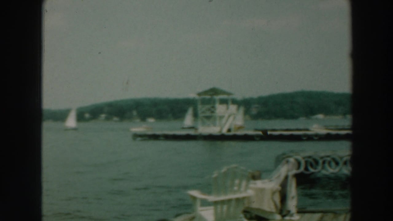 Dockside view of sailboats, a pier, white chairs, and a tower beside a lake.