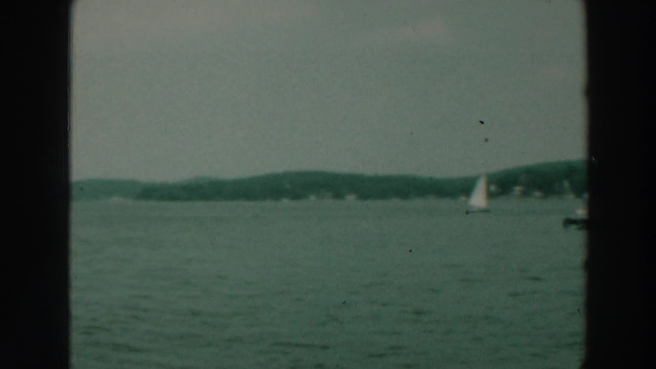 Open lake with a sailboat near the right edge and low shoreline in the distance.