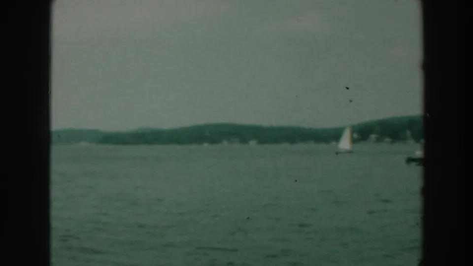 1964 Lake Winnebago view over open water with a small sailboat, distant wooded shore, and dark film frame edges.