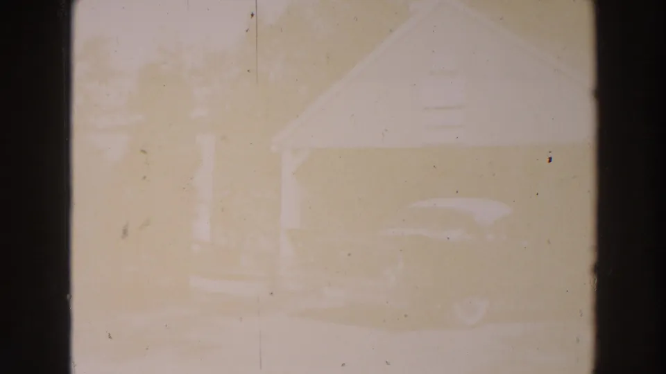 A mid-century car sits near a small gabled building by Lake Winnebago in faded 8mm footage.