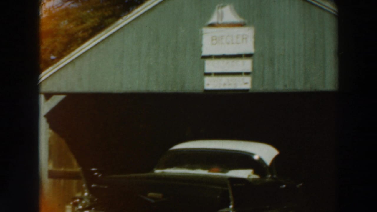 Dark vintage car with a white roof parked beneath a green garage with a BIEGLER sign.