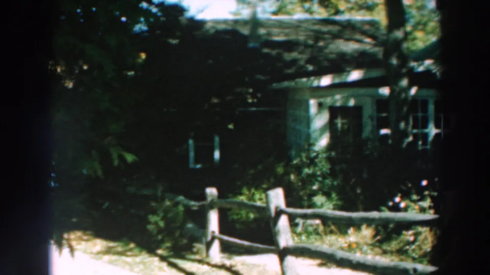 Shaded frame of the Lake Winnebago house exterior, with fence posts, trees, and foliage partially obscuring the windows.