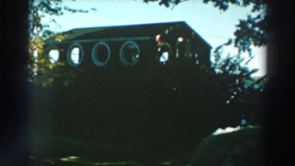 1964 Lake Winnebago frame showing a dark wood house facade with round windows, trees, and visible water.