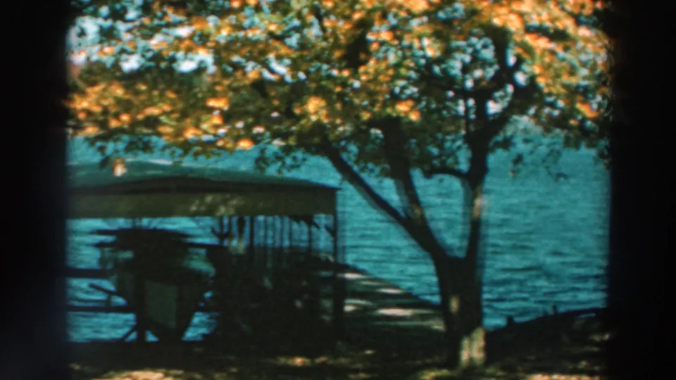 1964 Lake Winnebago view of a covered dock or boat shelter beneath autumn trees with open water behind it.