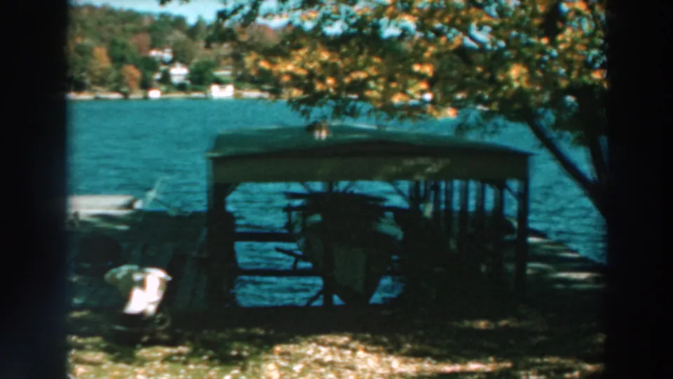 Lake Winnebago shoreline in 1964 with a covered shelter, dock, blue water, early autumn foliage, and houses across the lake.