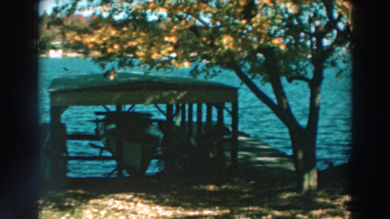 Covered dock beside blue lake water, framed by leafy trees and film gate edges.