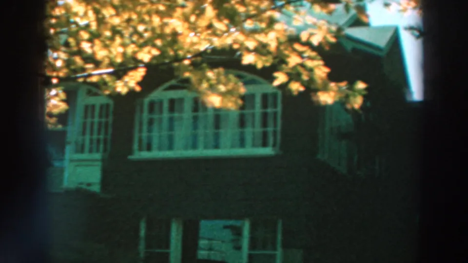 1964 Lake Winnebago frame showing a closer portion of the house exterior, with white-framed windows, a door, and golden leaves overhead.