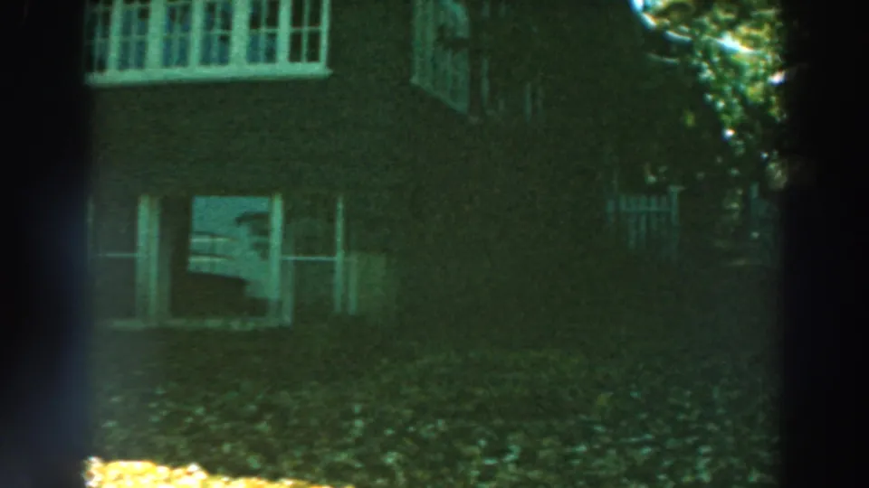 1964 Wisconsin home-movie view of a brick house facade, white-trimmed windows, lawn, and leafy yard.
