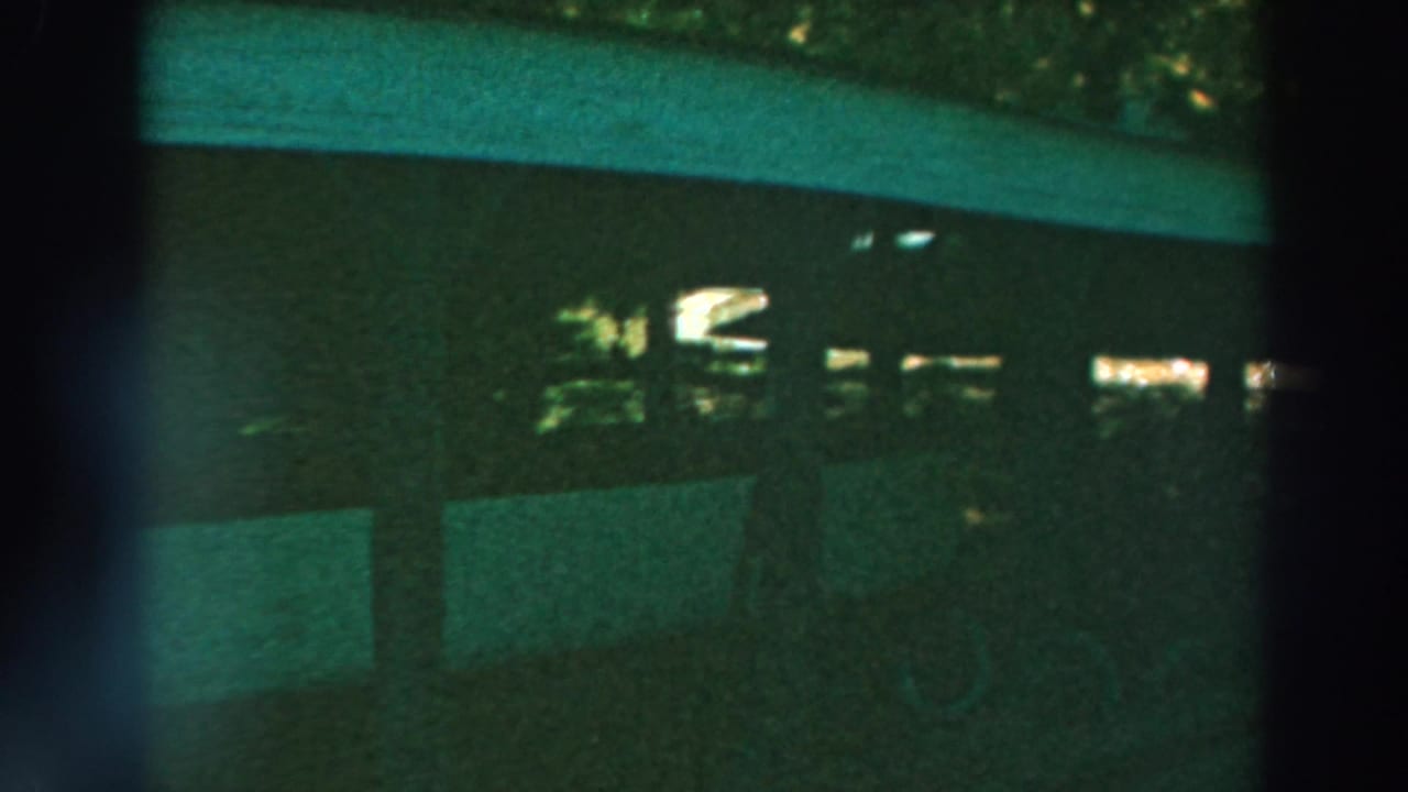 1964 Lake Winnebago 8mm frame showing a dim stable-like interior with dark posts, rectangular panels, and faint light beyond.