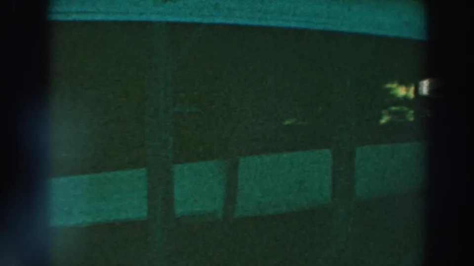 Green-tinted 8mm frame from Lake Winnebago showing dark barn or stable partitions, vertical posts, and a small bright area at night.