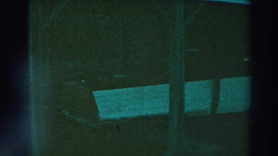 1964 Lake Winnebago 8mm frame showing a shadowed stable or barn interior with vertical supports and pale rectangular panels.