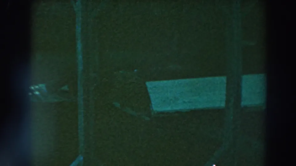 1964 Lake Winnebago home-movie frame showing the dim underside of a wooden pier and a partially visible white boat hull.