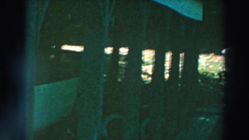 The camera looks across the shadowed pier structure toward bright openings and the white boat stored under the dock.