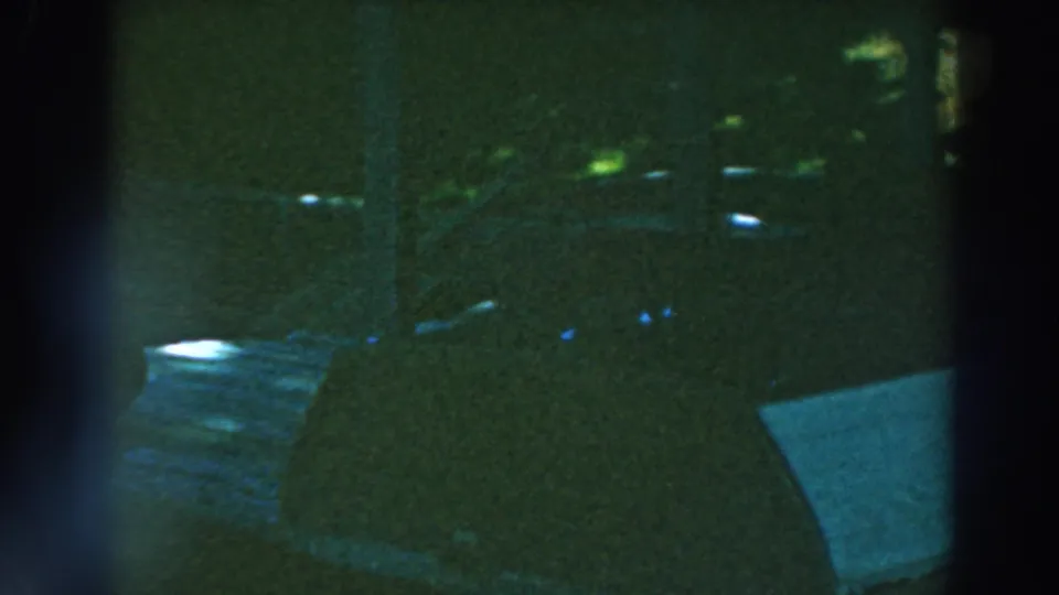 Dark 8mm frame from the Lake Winnebago clip showing a partial window view, dock boards, water, and shaded shoreline forms.
