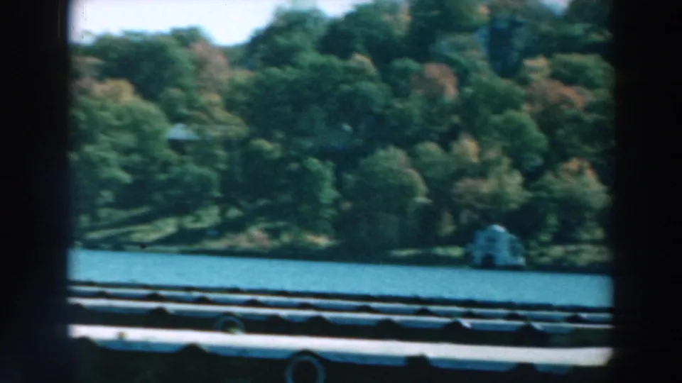 1964 Lake Winnebago frame with a clearer view of dock structure, blue lake water, wooded shoreline, and bright sky.