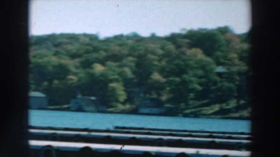 1964 Lake Winnebago boat view showing blue water, tree-covered shore, and small distant structures through soft 8mm focus.