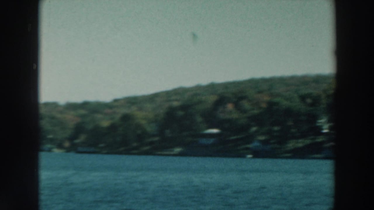 1964 Lake Winnebago view from a moving boat, with blue water, wooded shore, pale sky, and dark frame edges.