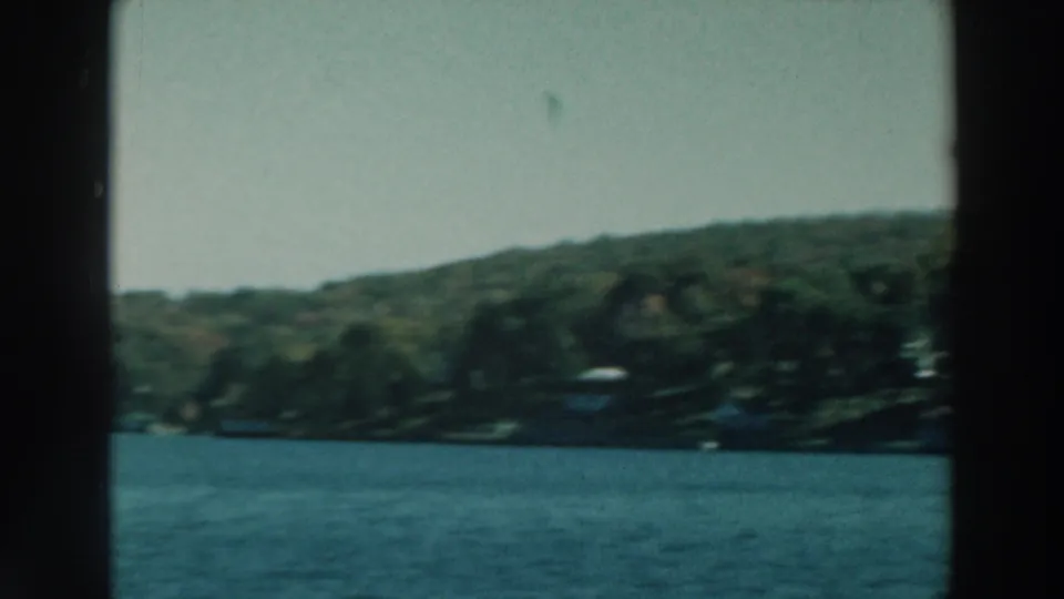 1964 Lake Winnebago view from a moving boat, with blue water, wooded shore, pale sky, and dark frame edges.