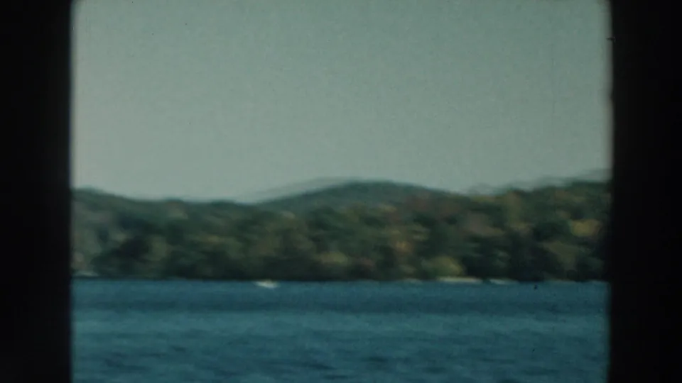 Soft 8mm view of Lake Winnebago with blue water, low wooded hills, and a faint shoreline from a moving boat.
