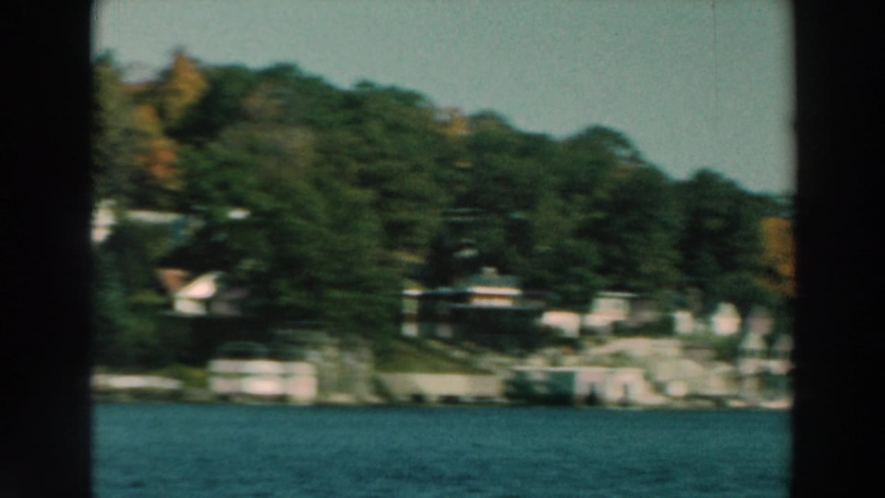 Houses and trees along a shoreline seen across blue lake water.
