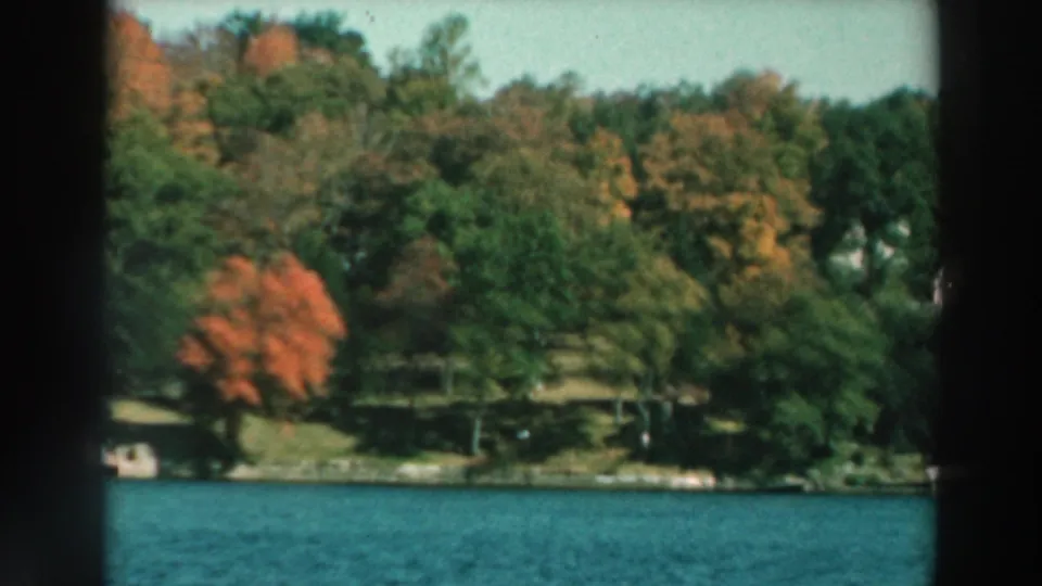 1964 Lake Winnebago view with autumn trees, green shoreline, and water in the foreground.