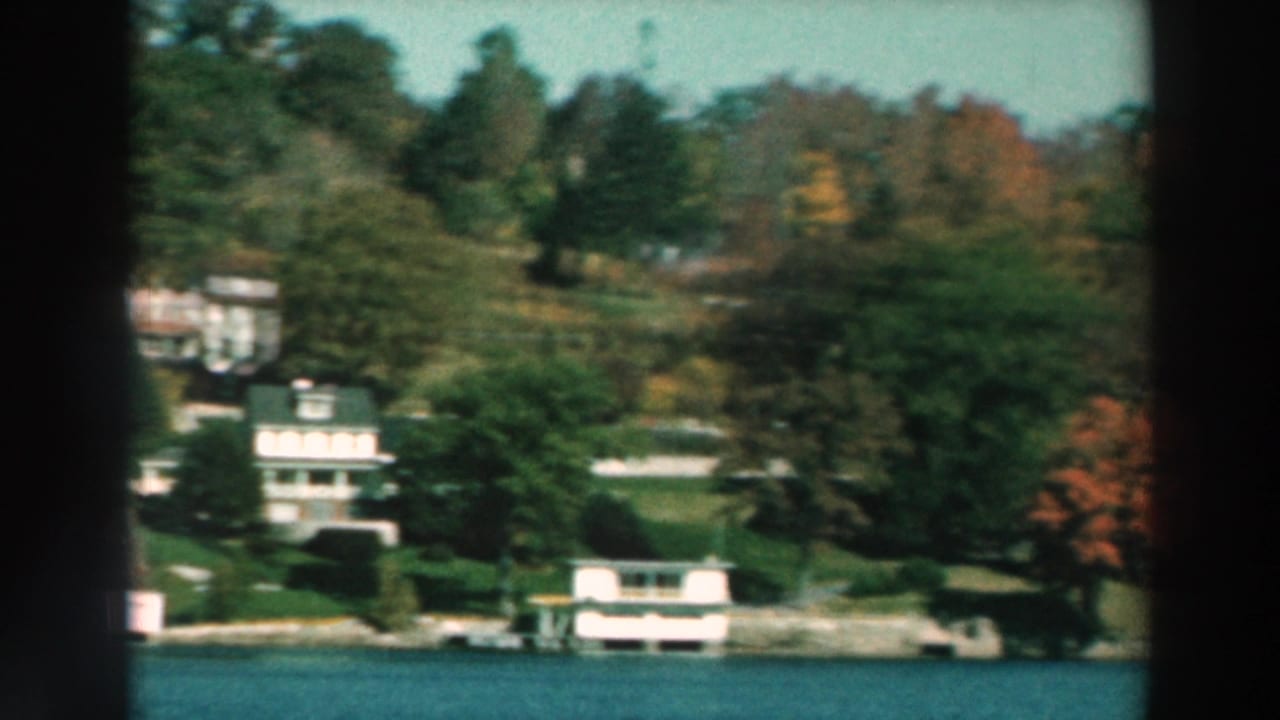 Lakeside homes and trees seen across blue water through dark film-frame edges.