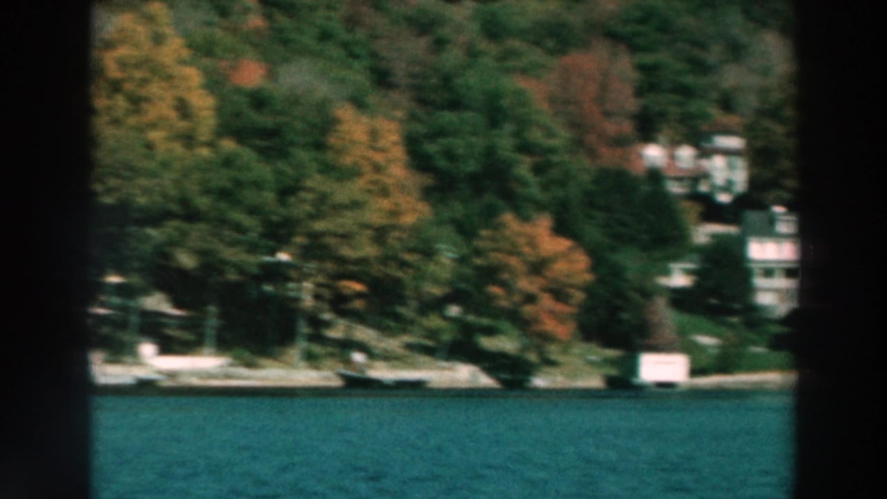 Lake Winnebago waterfront with scattered houses, docks, and dense autumn trees along the shore in 1964 home-movie footage.
