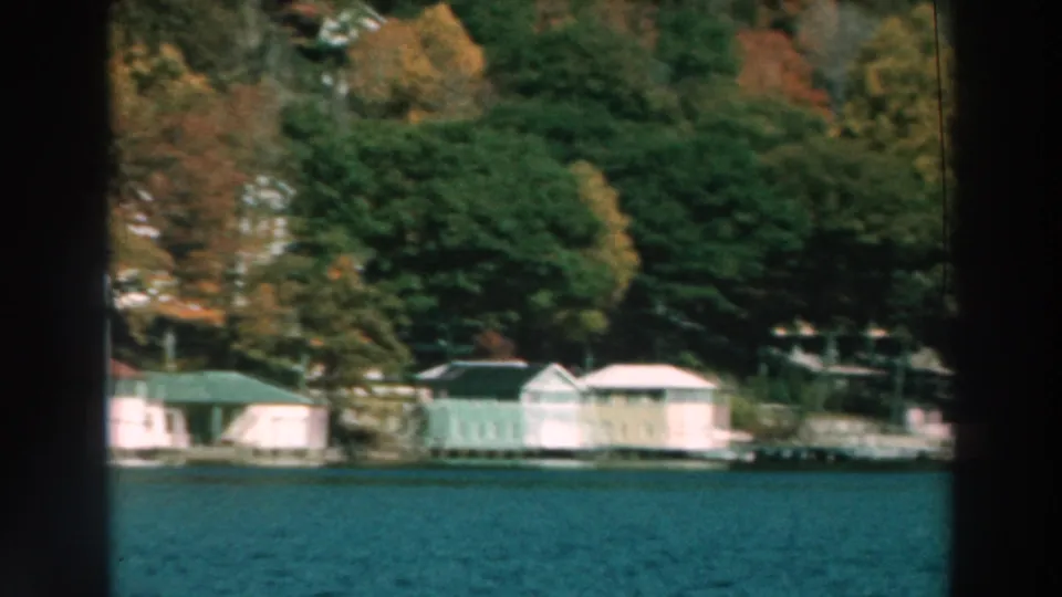 1964 lakeside view showing boathouses or waterfront buildings, docks, trees, and Lake Winnebago water from a passing boat.