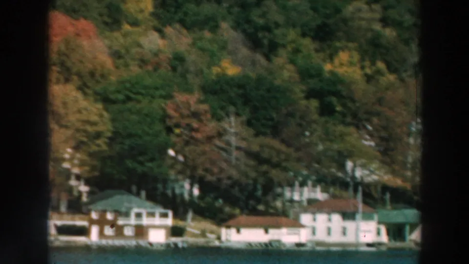 Lake Winnebago shoreline homes and boathouses appear below a wooded hillside with early autumn color in 1964 8mm footage.