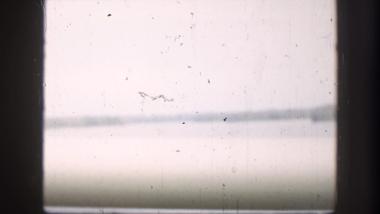 1958 8mm view from inside a vehicle, looking through a window toward hazy river water and a distant shoreline.