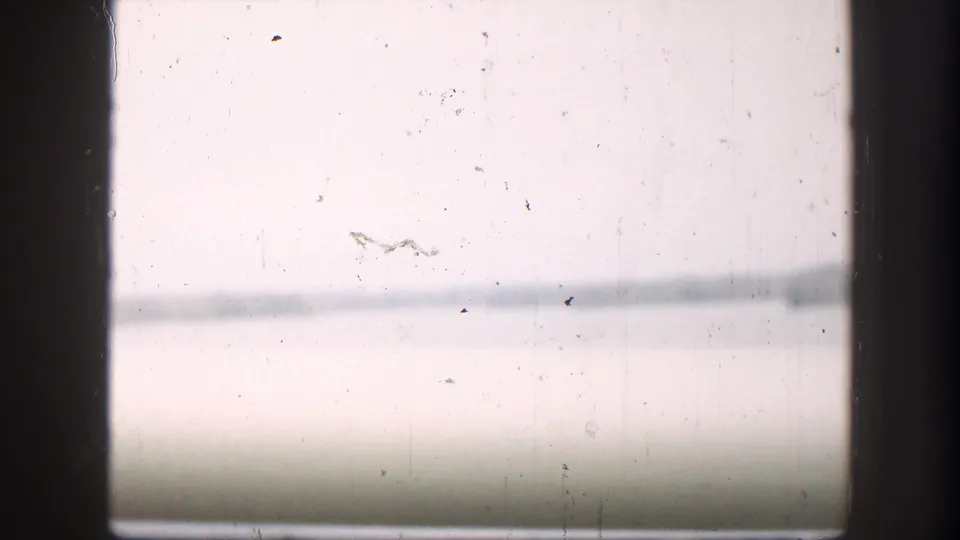 1958 8mm view from inside a vehicle, looking through a window toward hazy river water and a distant shoreline.