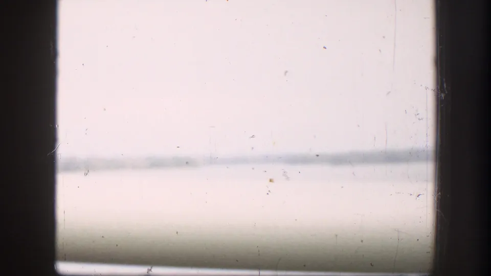 A soft 8mm passenger-window view shows a wide river and distant bank during the bridge crossing.