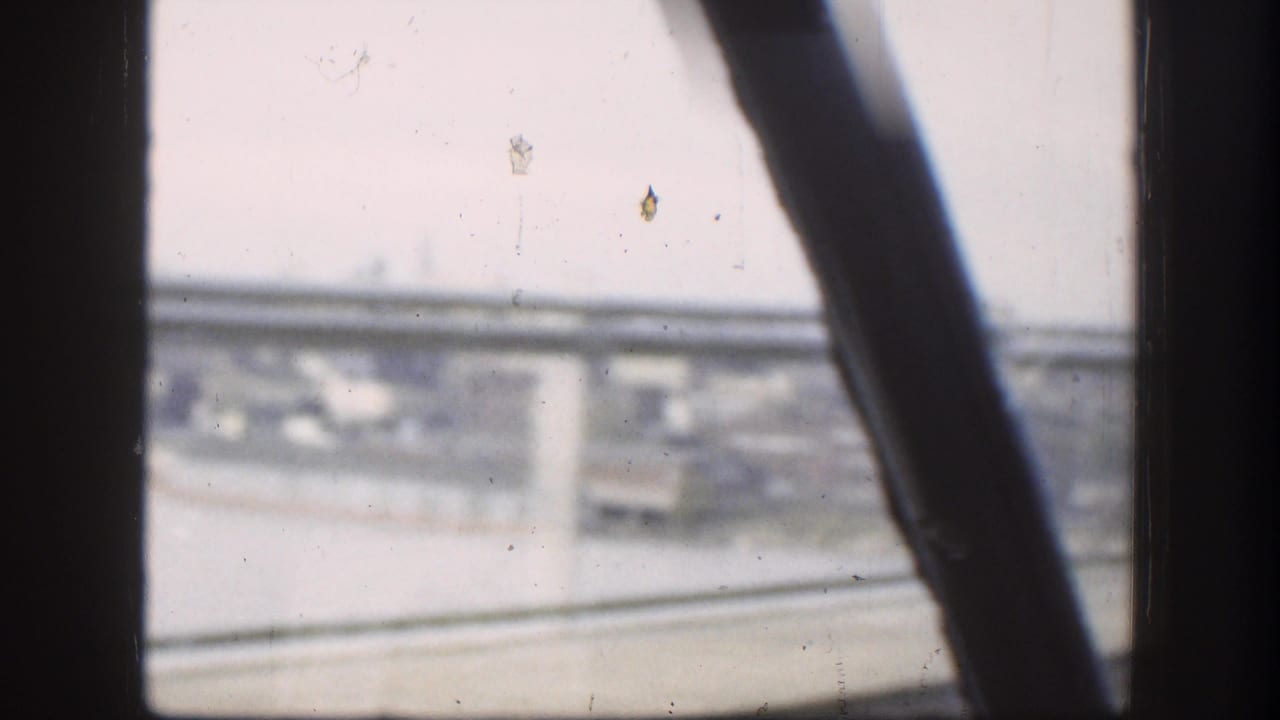 Forward view through a car window toward a bridge and distant urban area.