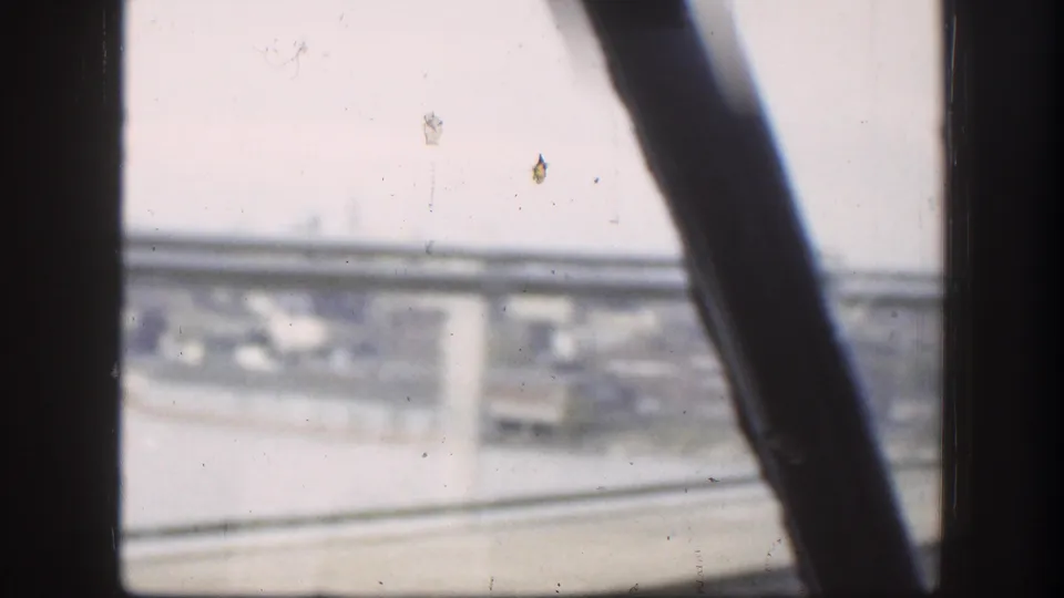 1958 Kansas home-movie frame looking through a vehicle window toward a bridge, road, and hazy urban background.