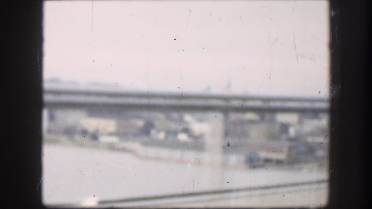 Bridge span and roadway seen through a dark vehicle window frame.