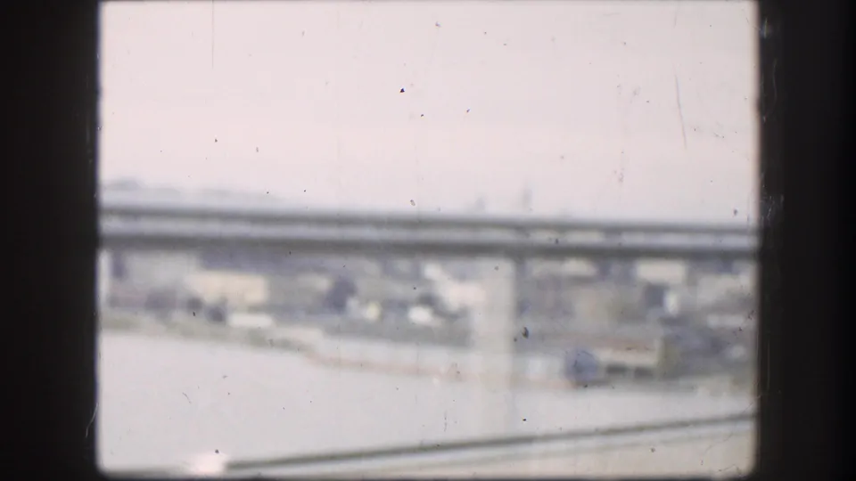 Soft 8mm view from inside a moving car, with bridge supports, road surface, and distant Kansas urban landscape visible.