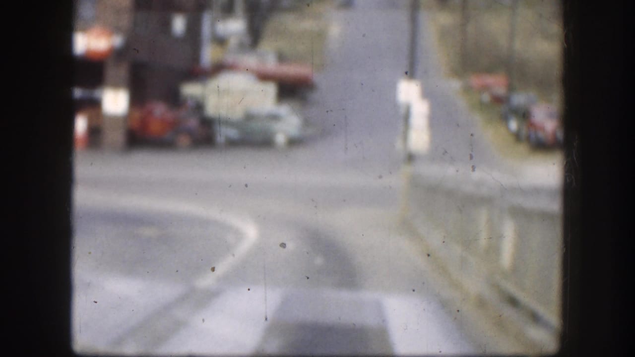 Soft street view through dark frame edges with parked cars and a curving road.